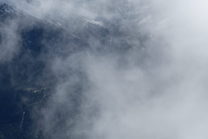 Snowy mountain peaks partially obscured by swirling white clouds and mist.