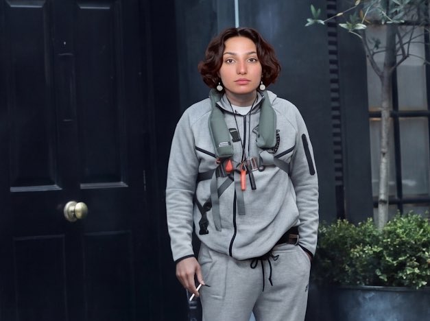 A woman stands outside a dark door with a green snakeshaped life vest draped around her neck, styled as a Medusa reference. The image plays on the Mythology of Medusa, whose hair was made of snakes, to humorously reset the algorithm as mentioned in the post.
