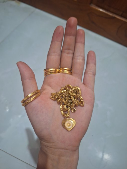 A hand displays two gold rings on the fingers and a collection of gold chain and pendant pieces resting in the palm.