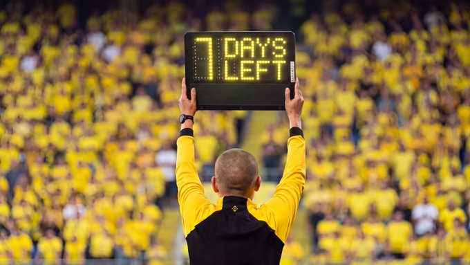 A person in a yellow and black jacket holds up an LED sign displaying "7 DAYS LEFT" amid a stadium crowd dressed in yellow, visually reinforcing the post's message that only one week remains before the trading competition's final whistle.