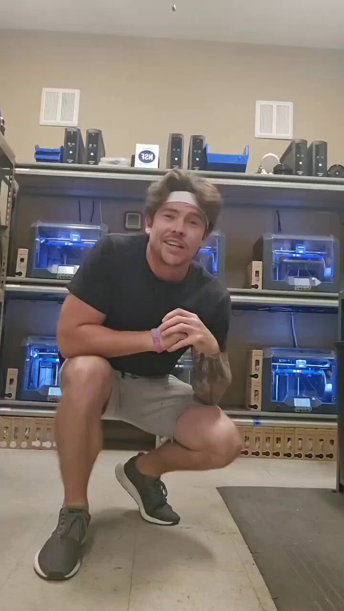 This image features a man posing for a picture while squatting down with his arms resting on his knees, wearing headphones or earbuds around his neck, which suggests he may be listening to music or an audio track during his workout session. The surrounding background appears to be related to weight training equipment, indicating that the man is in a fitness-oriented environment.
