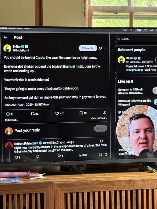 A TV screen showing an X/Twitter post by @GodsBurnt urging followers to buy crypto, with replies visible underneath.
