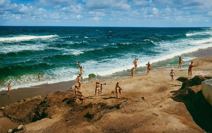A group of people enjoy a sunny day at a rocky coastline with crashing ocean waves, fitting the "Breaking The Waves" theme mentioned in the post. No text or identifying numbers are visible in the scene, which captures swimmers and beachgoers along a rugged shore.