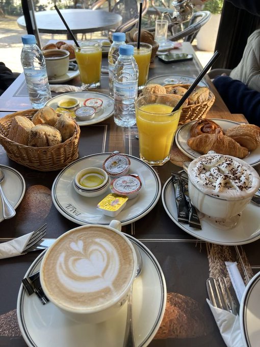 A luxurious breakfast spread featuring lattes with heart latte art, fresh orange juice, croissants, and jam sits on a table at "FIVE" hotel, with a sugar packet reading "FIVE" visible—evoking a relaxed, indulgent morning that contrasts with the "big things coming" excitement mentioned in the post.