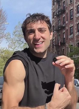 A man in a black sleeveless shirt smiles outdoors on a city street, pointing at himself while posing for a selfie—visually embodying the "JUST IN" announcement in which RASMR reveals $RAYCAT as his highest conviction Stonkfun play, explaining that Stonkfun's success directly benefits Raydium through automatic pool deployment.