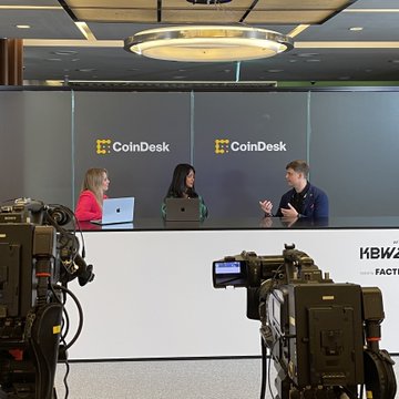 A man in a yellow sweater discusses AI agent security on CoinDesk's live broadcast alongside hosts Jenn Sanasie and Eleanor Terrett at #KBW2026, with the backdrop displaying the "CoinDesk" logo and partial "KBW" branding visible on the set.