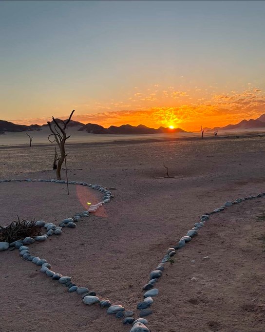 The image shows a beautiful sunrise over a desert landscape, with the sun rising behind mountains in the distance. The sky is painted in shades of orange and yellow as the sun sets below the horizon. In the foreground, there are rocks arranged in a circular pattern, possibly part of an art installation or a symbolic representation of unity and harmony within nature. The post about "Good morning Homies @quipnetwork" suggests that this image might be related to a social media post promoting environmental awareness or highlighting the beauty of natural landscapes.