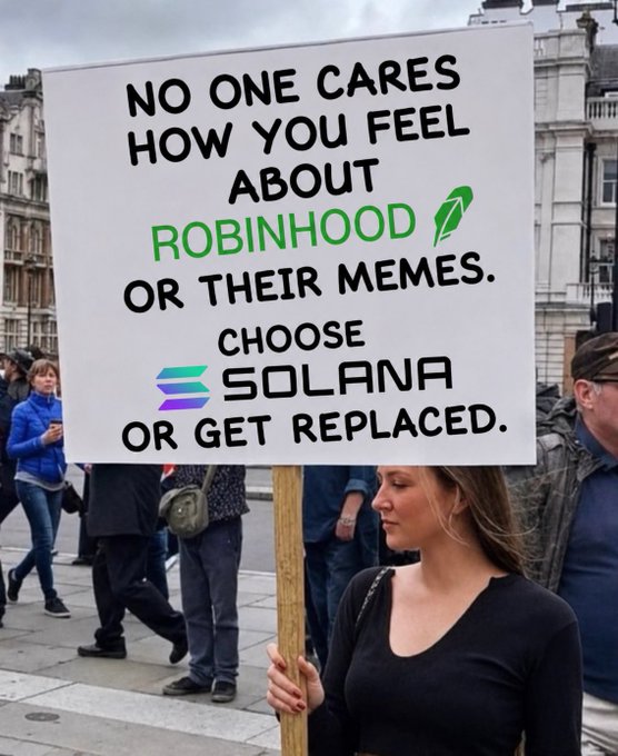 A woman holds a protest sign reading "NO ONE CARES HOW YOU FEEL ABOUT ROBINHOOD OR THEIR MEMES. CHOOSE SOLANA OR GET REPLACED."