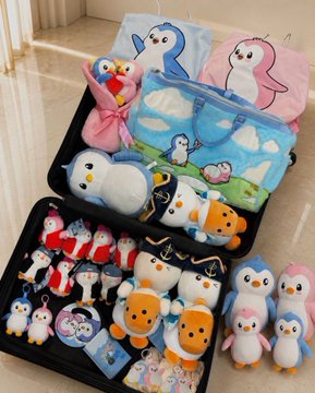 An open black suitcase packed with various plush toys, including penguins, birds, and cartoon characters, arranged neatly in both compartments.