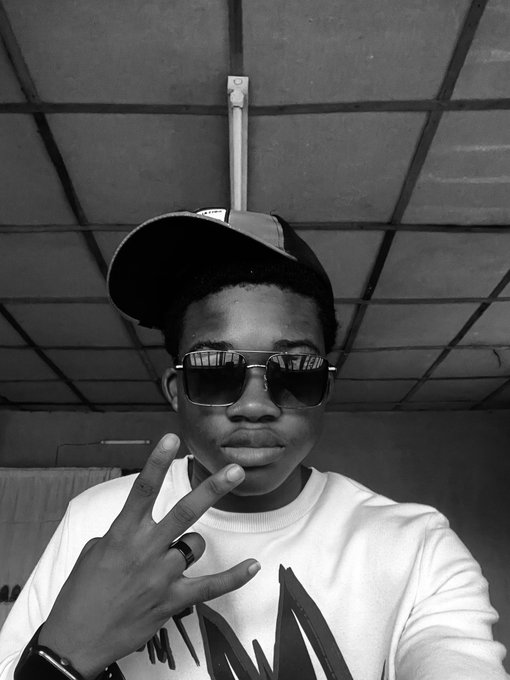 A black-and-white photo of a young man wearing a cap and aviator sunglasses, holding up a peace sign.