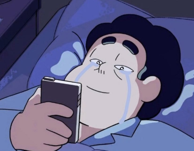 An anime character lying in bed with tears streaming down his face while smiling and looking at his smartphone.