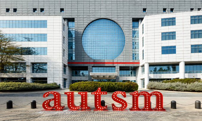 A modern building features a large circular window above its entrance, with the word "autism" displayed in large red illuminated letters in front.