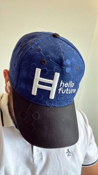 A close-up view of a person wearing a navy blue and dark gray baseball cap featuring a white 'H' logo and the text 'hello Future,' with the cap displaying a molecular or network pattern across the fabric.