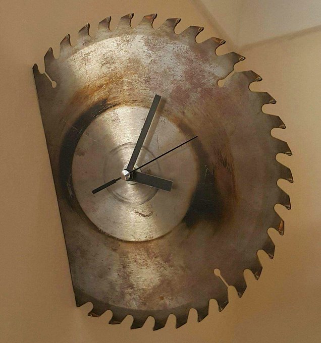 A wall clock designed to resemble a large, weathered circular saw blade with three black clock hands mounted in the center.