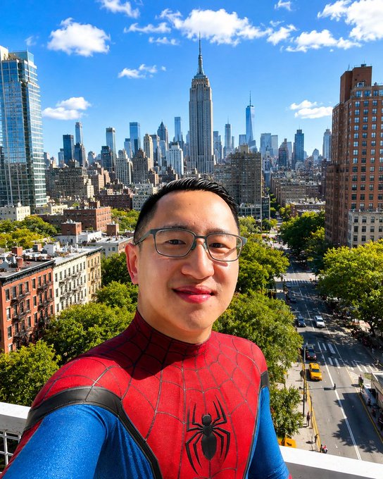 A selfie of a man wearing glasses and a Spider-Man costume with a city skyline featuring the Empire State Building in the background.