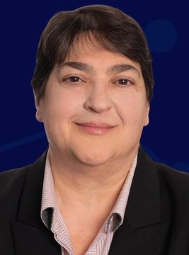 The image features a woman wearing a black blazer with white stripes. She has short hair and a smile on her face as she looks directly at the camera. The background of the photo is blue, which contrasts nicely with the woman's outfit. There are no texts or other objects in the image, making it a simple yet visually appealing composition that highlights the subject - the woman wearing the black blazer with white stripes and looking directly into the camera.