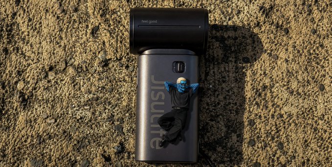 A miniature figurine wearing a white helmet and dark clothing lies relaxed on top of a black 'insitra' branded device, possibly a power bank or speaker, resting on a concrete surface.