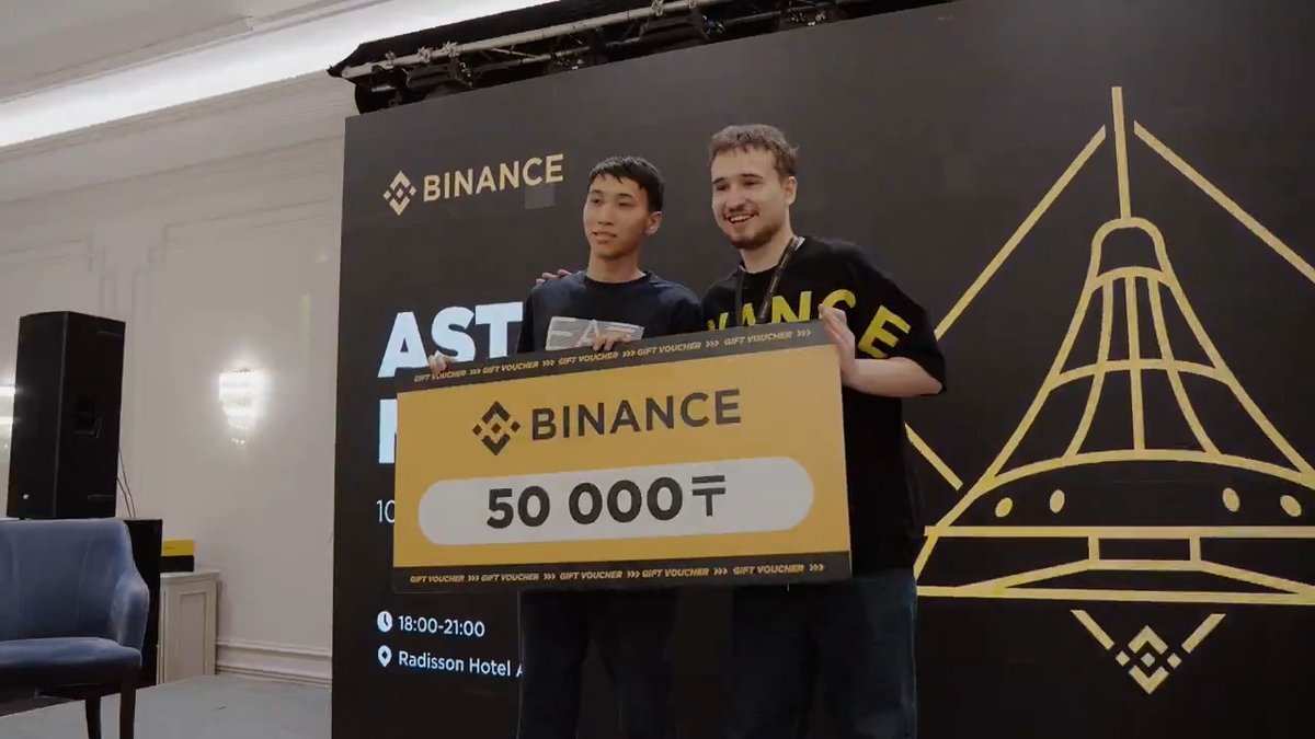 Two men proudly display an oversized Binance gift voucher worth 50,000₸ on stage at the Radisson Hotel during a Binance crypto education event in Kazakhstan. The check presentation captures the community-focused spirit described in the post, highlighting the prizes given away to the 400+ attendees at this engaging crypto meetup in Astana.