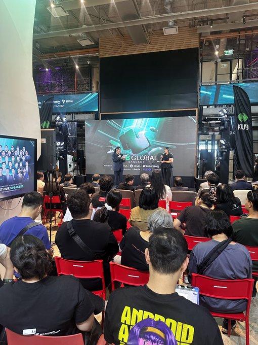 An audience sits in red chairs facing a stage with a large screen displaying 'GLOBAL TECH WEEKEND' logos for Tech in Asia and UNDP, while two speakers present.