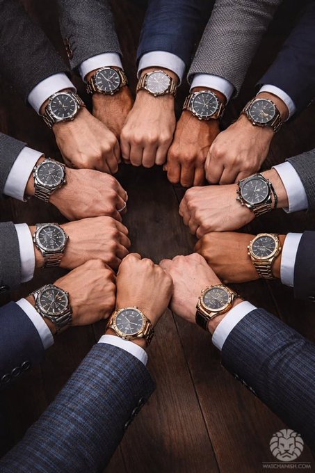 A circle of men's hands, each wearing a luxury watch and dressed in suits, come together in a fist-bump huddle on a wooden surface, embodying the "gm gangsters" solidarity and motivation for the day's grind. The watermark "watchismo.com" appears in the bottom right corner.