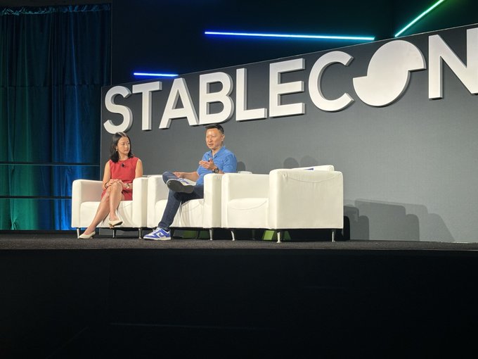 Two people sitting in white armchairs on a stage during a panel discussion at the STABLECON conference, with the event logo displayed on a large screen behind them.