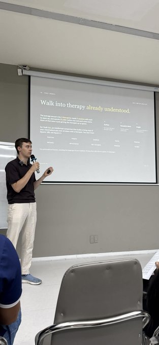 A man presenting in front of a projection screen displaying a webpage titled 'Walk into therapy already understood,' with partial audience members visible in the foreground.
