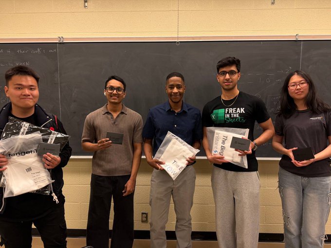 The image shows five young men holding up their college acceptance letters or cards, possibly from the University of Waterloo. They are standing together against a blackboard background, which suggests that they might have just received their acceptance letters or cards for their studies at the university. The group appears excited and proud as they share this moment with each other.