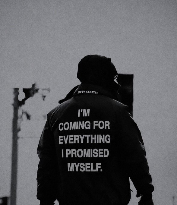A black and white photo of a hooded figure seen from behind, wearing a jacket with 'NINETY KARATE' and the text 'I'M COMING FOR EVERYTHING I PROMISED MYSELF.' printed on the back.