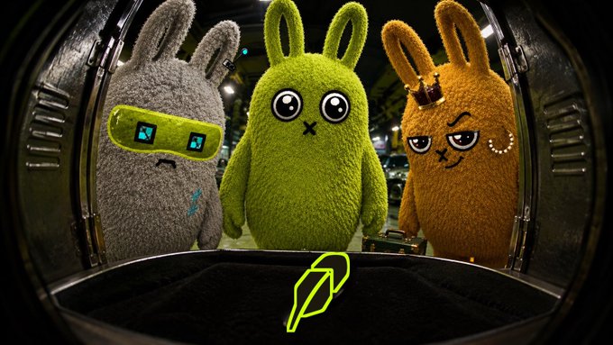 Three fuzzy bunny characters—one gray with a tech visor, one green, and one brown with a crown—peer through a hatch alongside a yellow feather logo, tying into the @BunnysHood drop promotion offering 10 GTD spots for an EVM wallet.
