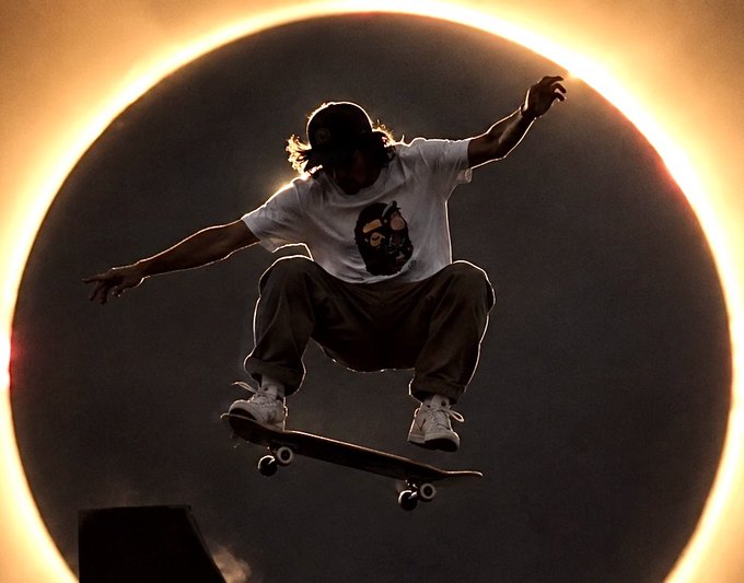 A silhouette of a skateboarder performing an aerial trick against a dramatic circular ring of bright light.