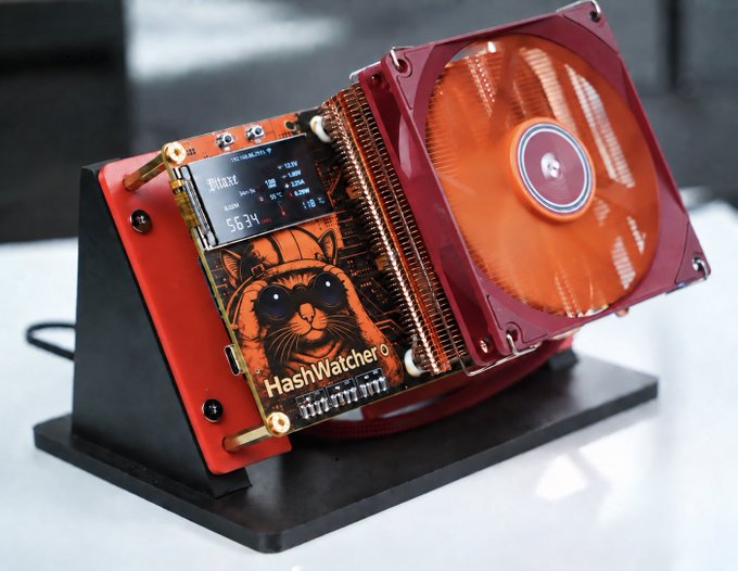 A red and orange computer graphics card with a large orange fan, displayed on a stand, featuring a sticker of a cat with sunglasses and the text "HashWatchero".