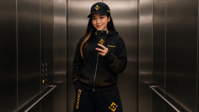 A person wearing Binance-branded apparel, including a black cap, hoodie, and pants featuring the Binance logo and "BINANCE" text, takes a selfie in an elevator. The image visually matches the post's caption, showcasing branded swag from the cryptocurrency exchange.