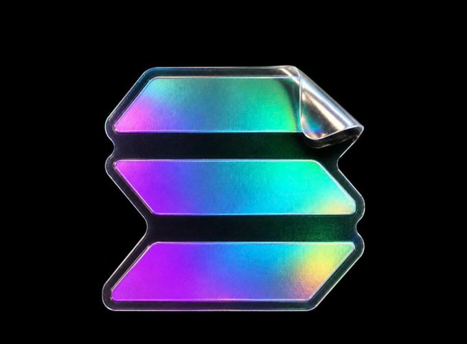 A holographic rainbow sticker shaped like three stacked bars peels at the top right corner against a black background, visually representing the $ANSEM token logo to match the post about getting a birthday cake themed around the memecoin.