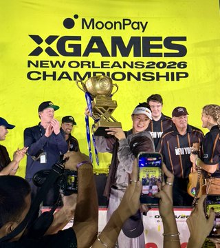 A celebratory moment captured at the X Games New Orleans 2026 Championship, where a team of athletes wearing "New York" jerseys proudly hoists a large trophy in front of a yellow MoonPay-branded backdrop. Fans surround them, snapping photos with their phones to commemorate the victory.