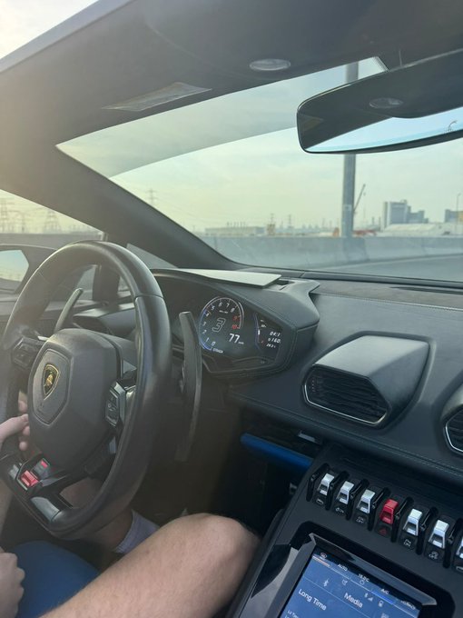 A driver's view from inside a Lamborghini with the dashboard showing 77°F and "Long Time" on the infotainment display, ready to tackle "a new day to Win."