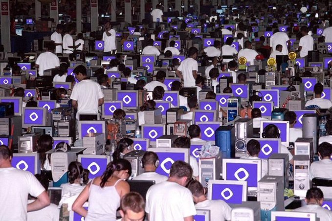 A massive LAN party fills a large hall with hundreds of participants, mostly dressed in white shirts, sitting at rows of glowing blue monitors displaying a distinctive circular "G" logo (Gamers Gate/ASUS) on each screen, suggesting a large-scale gaming tournament or esports event. The image evokes the "destination arrives all the same" meme, humorously implying that no matter how players try to avoid it, they're inevitably drawn to the event like destiny.