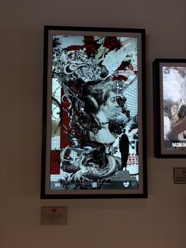 A framed digital artwork displayed at the "Beyond Silence" Exhibition by OneLoveArtDAO, featuring intricate black, white, and red abstract figurative compositions with a small plaque below identifying it as part of the showcase.