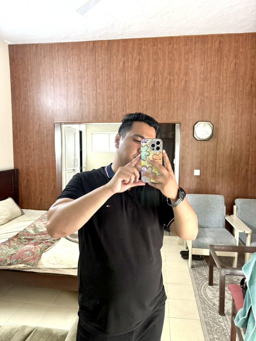 A man takes a mirror selfie in a bedroom, holding a phone with a floral case that covers his face, while giving a small hand gesture. The casual, upbeat pose complements the post's cheerful "GOOD MORNING EVERYONE" greeting and weekend vibes, though the image itself contains no visible text or numbers related to the "Big Win" theme.