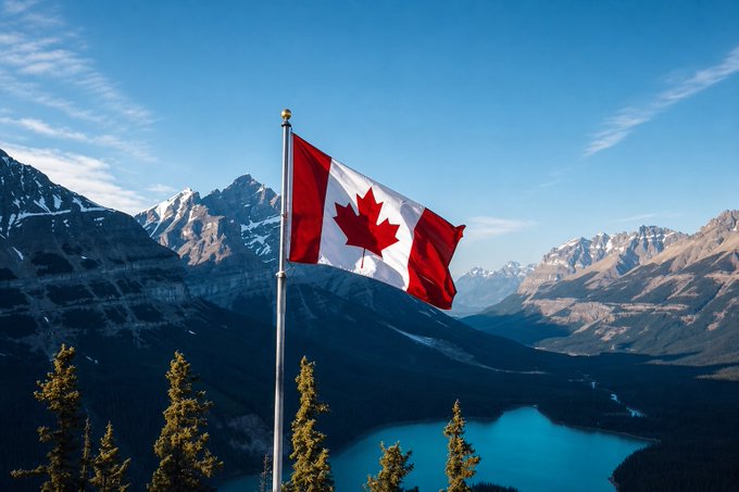 The Canadian flag waves prominently against a backdrop of snow-capped mountains and a turquoise lake under a clear blue sky.