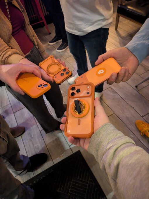 Four people holding phones with matching bright orange cases in a circle.