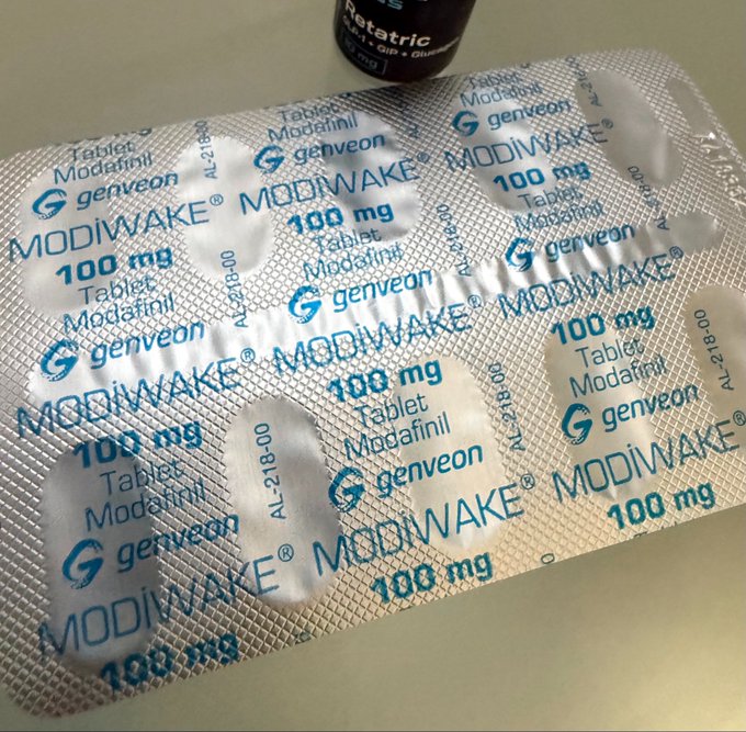 A blister pack of MODIWAKE 100 mg Modafinil tablets manufactured by Genveon, with an empty blister pocket visible.
