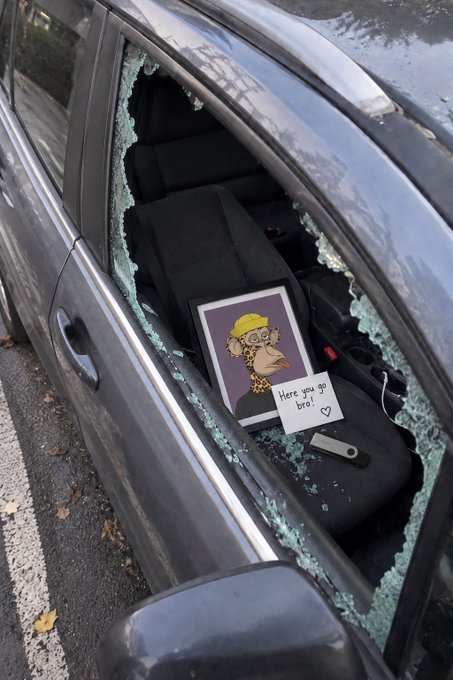 A car with a shattered window displays a framed cartoon drawing of a giraffe wearing a hard hat, accompanied by a handwritten note reading "Here you go bro!" with a heart, humorously suggesting that someone named BorisVagner left the picture for the car's owner after breaking in.
