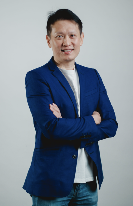 A man in a navy blazer and white t-shirt stands with arms crossed against a light background, smiling—representing Binance CEO Richard Teng, who announced that Binance assisted India's NCB in tracing cryptocurrency transactions and dismantling a major darknet drug network.