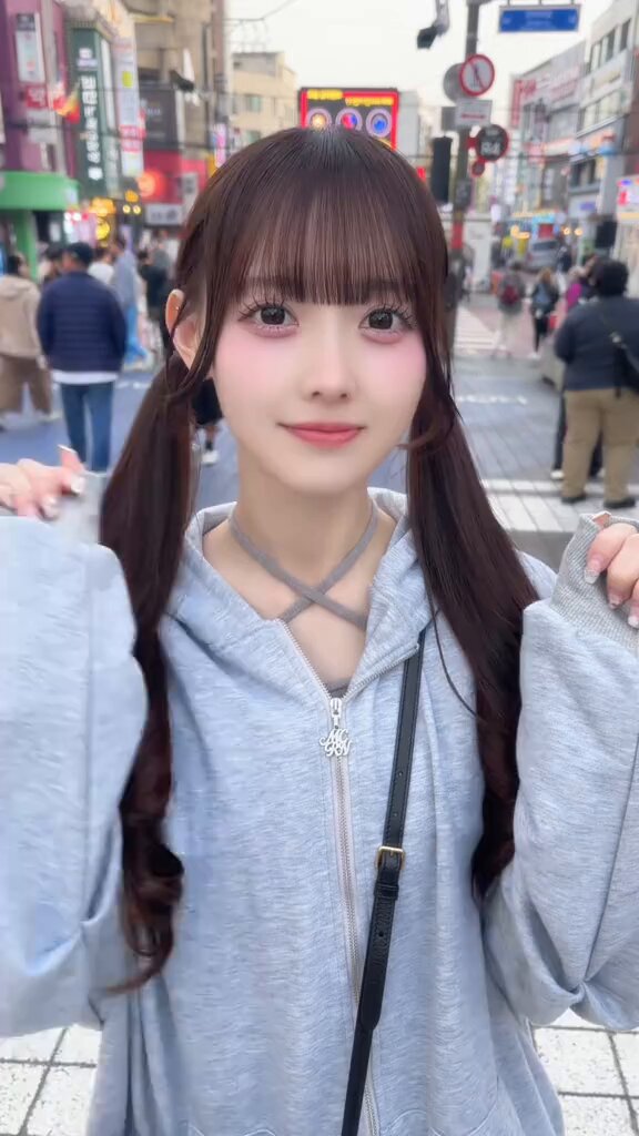 The image features a young woman with long hair wearing a grey hoodie, posing for a photo while holding her hair back with two ponytails. The background of the picture shows a busy street scene with people walking around, indicating that she might be in an urban setting or at a public event. There is also a post on social media related to the image, which includes text such as "6.16梭哈晨报", "经历了一晚上又多亿的身价", and "1. $BTC 兜兜转转", which suggests that the photo might have been taken at a market or an event where people are selling items for various currency types, including Bitcoin.
