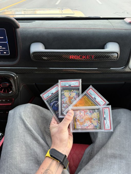 A person holds up a fan of four graded Pokémon cards in PSA slabs inside a Mercedes G-Wagon, with the dashboard displaying "ROCKET EDITION" — celebrating their newly graded cards back from PSA.
