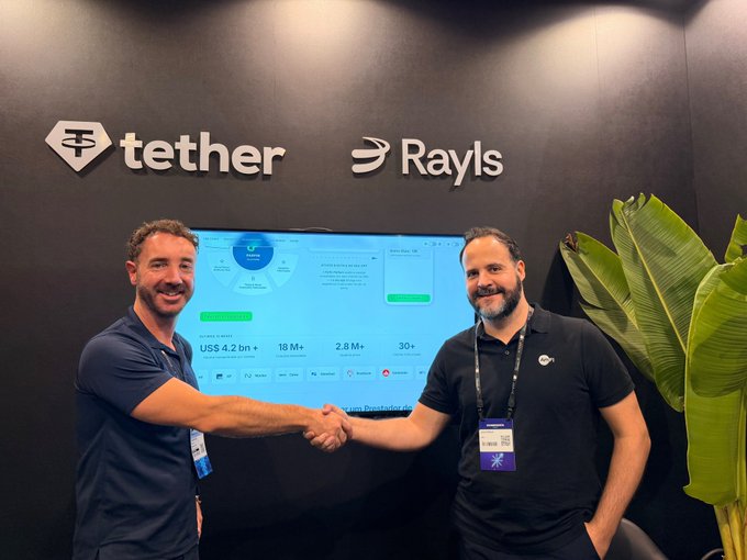 Two men shaking hands in front of a wall displaying the Tether and Rayls logos next to a screen showing company statistics.