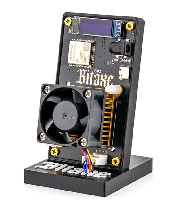 The image shows a Bitaxe 601, an open-source Bitcoin mining device featuring a small display, cooling fan, and exposed circuit board mounted on a stand. The "brb, gonna 51% attack LukeCoin" caption humorously references how this compact solo mining rig could theoretically be used to execute a majority hash rate attack on a small, low-security cryptocurrency network.