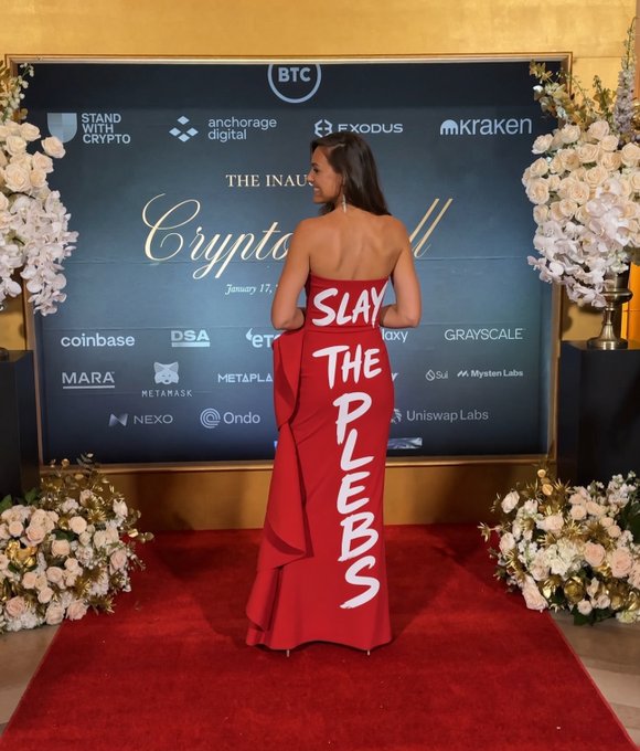 A woman in a strapless red gown stands on a red carpet at the "Inaugural Crypto Ball" (January 17), turning to reveal the words "SLAY THE PLEBS" hand-painted on the back of her dress. The backdrop features logos of major crypto companies including Coinbase, Kraken, MicroStrategy, Metaplanet, and Grayscale, tying the bold anti-critique message to the industry gathering — fitting for the post's jab at Michael Saylor's known critic-deflecting rhetoric.