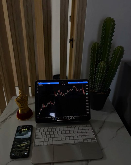 An iPad displaying a stock trading chart sits on a white marble desk with an Apple Magic Keyboard, next to a golden king chess piece, a phone showing 3:58, and a tall potted cactus.