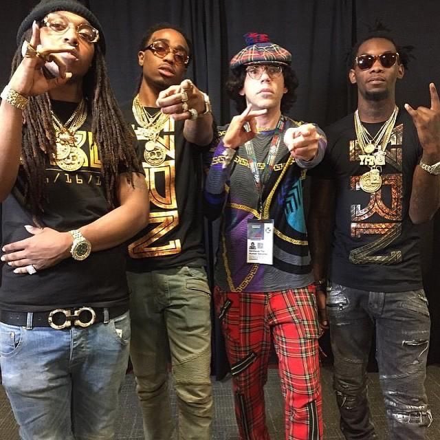 Four men pose confidently in matching black 'TRU' jerseys with gold accents, heavy gold chains, and sunglasses, with one wearing a flat cap and red plaid pants.